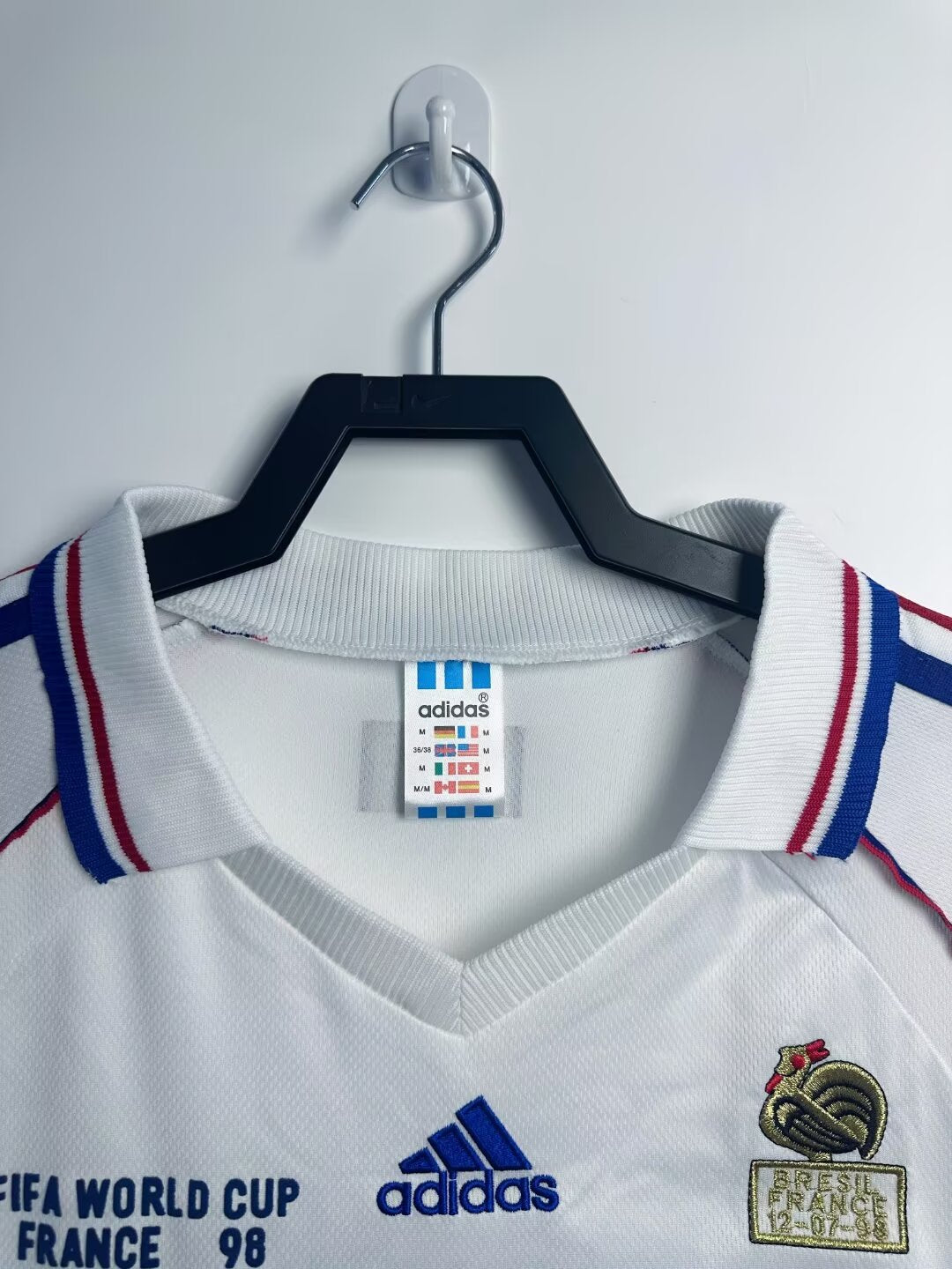 White sports jersey with Adidas logo on a hanger against a white background