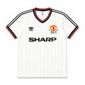 A white Adidas Manchester United home jersey with thin vertical pinstripes, featuring the black SHARP sponsor logo across the chest, the club crest on the right, and the black Adidas trefoil logo on the left. The collar and sleeve cuffs have black and red trim, and the sleeves feature black stripes.