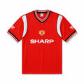 A red short-sleeve Manchester United soccer jersey by Adidas, featuring white side panels, black and white striped collar and sleeve cuffs, the Manchester United crest on the chest, and the white Sharp sponsor logo across the front.