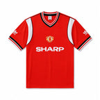 A red short-sleeve Manchester United soccer jersey by Adidas, featuring white side panels, black and white striped collar and sleeve cuffs, the Manchester United crest on the chest, and the white Sharp sponsor logo across the front.