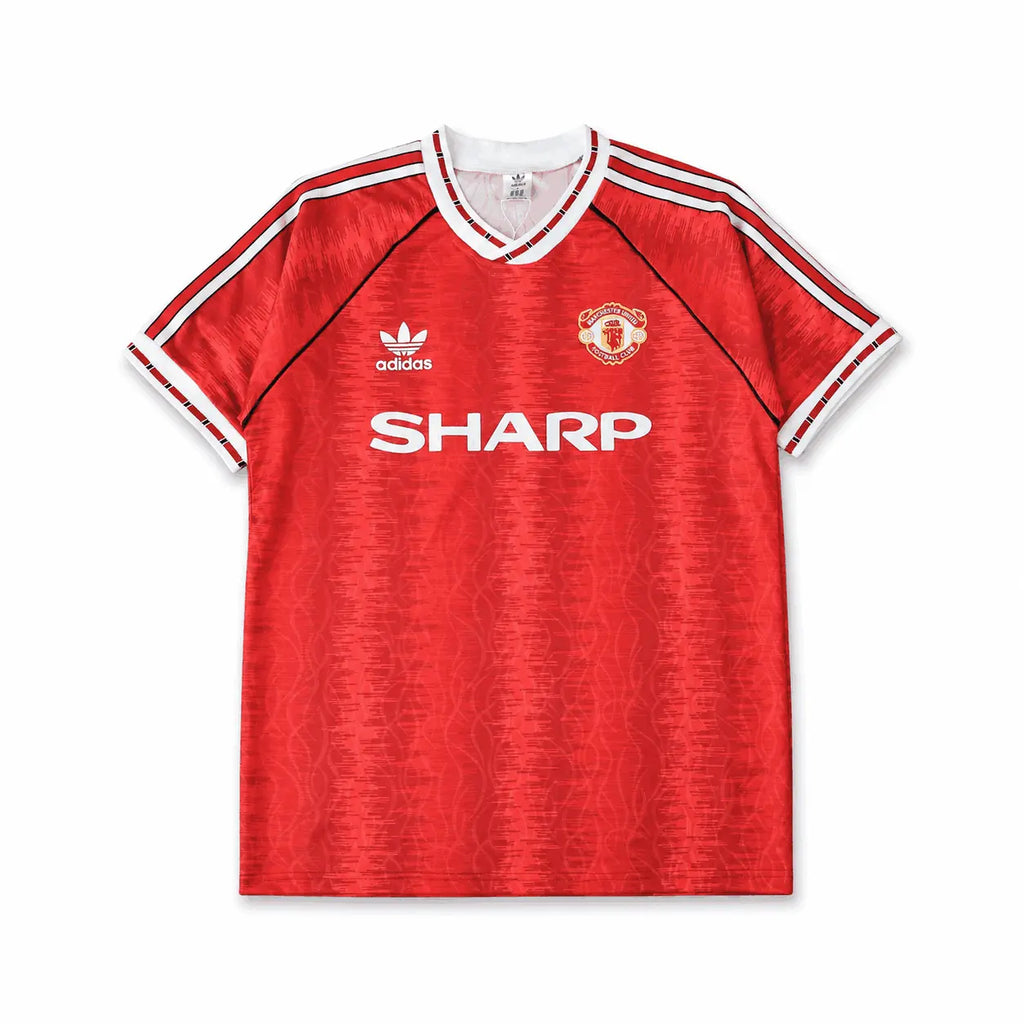 A red short-sleeve Manchester United soccer jersey, featuring white shoulder stripes, a white V-neck collar, the white logo, the Manchester United crest, and the white SHARP sponsor logo across the chest.
