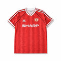 A red short-sleeve Manchester United soccer jersey, featuring white shoulder stripes, a white V-neck collar, the white logo, the Manchester United crest, and the white SHARP sponsor logo across the chest.