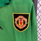 Green sports jersey with Manchester United logo on a chain-link fence background