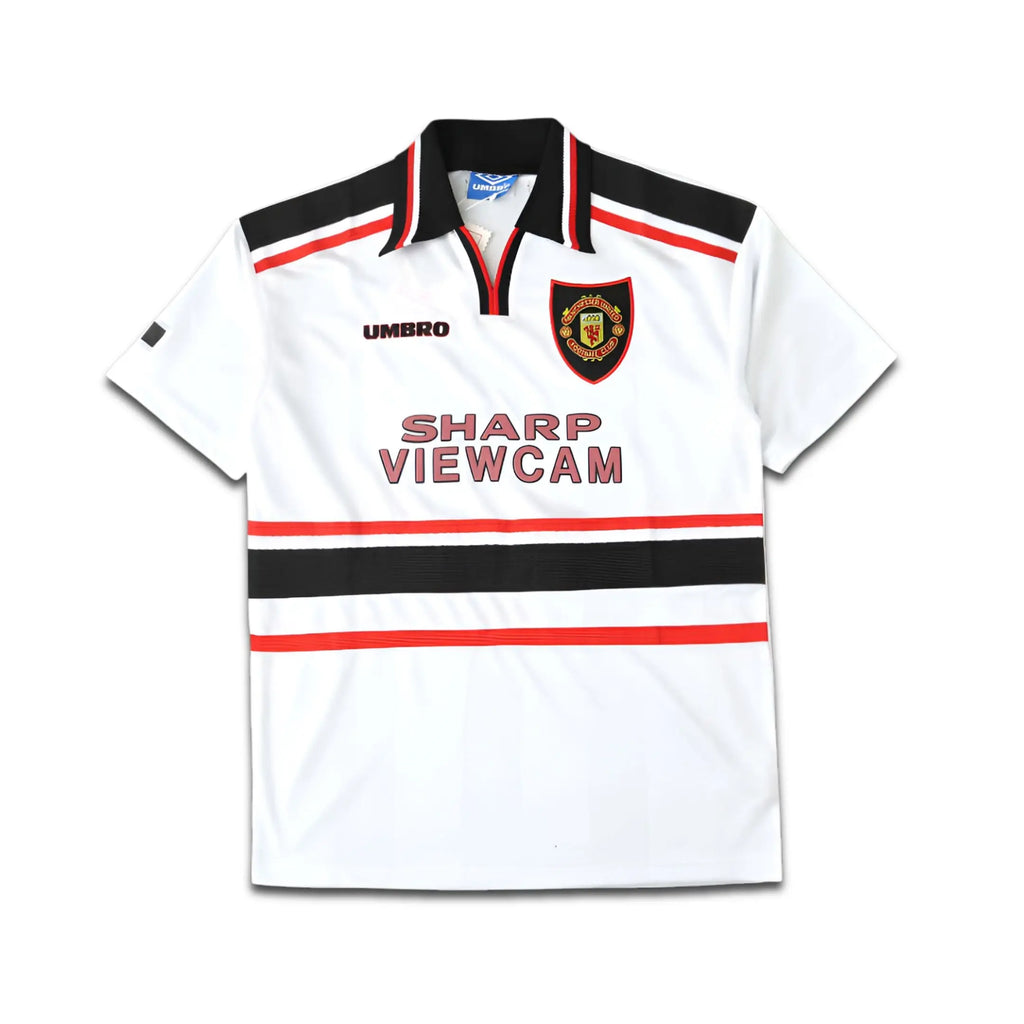 White Umbro Manchester United jersey with black and red accents, featuring a logo and text on a white background