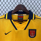 Yellow Arsenal sports jersey with a hanger against a chain-link fence background