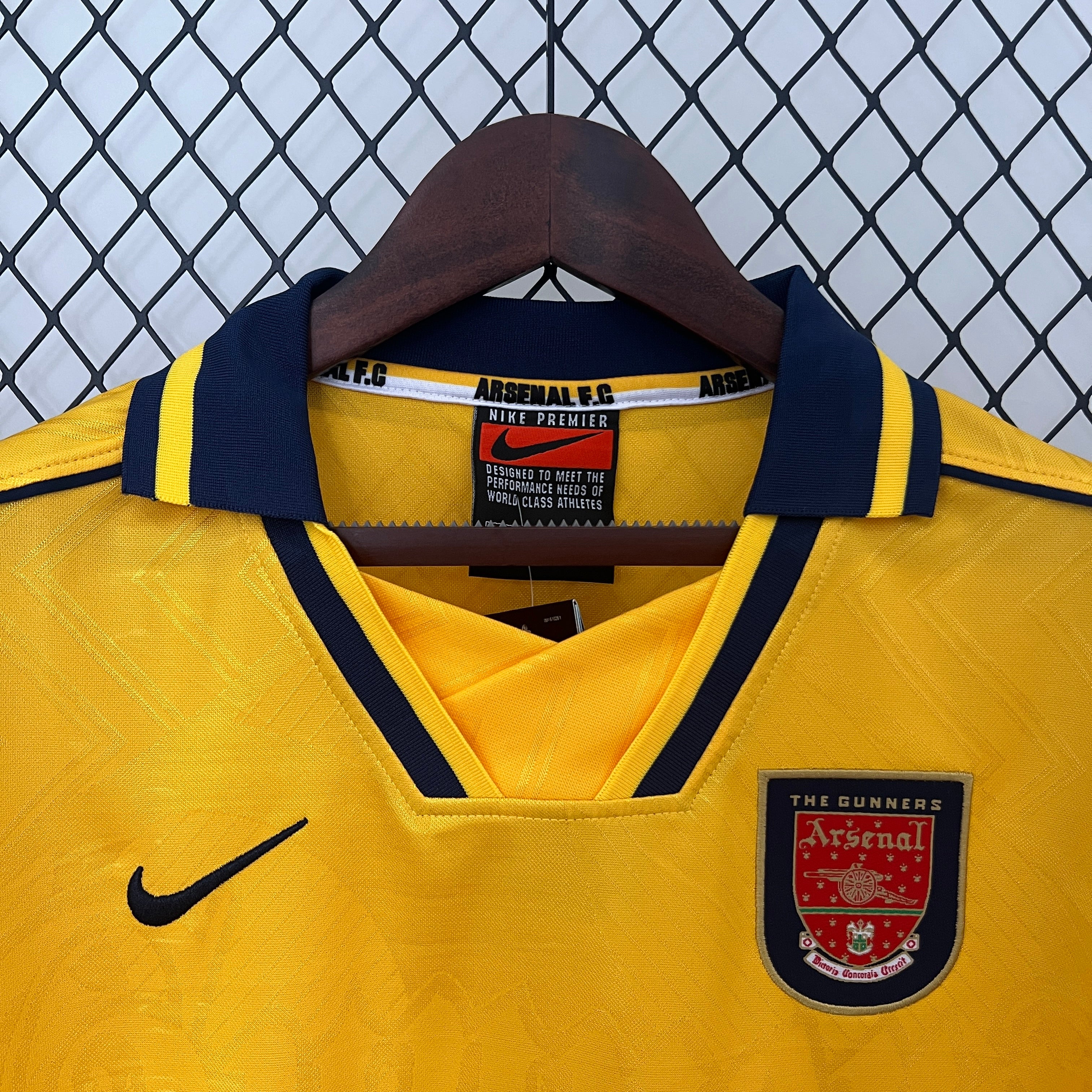 Yellow Arsenal sports jersey with a hanger against a chain-link fence background