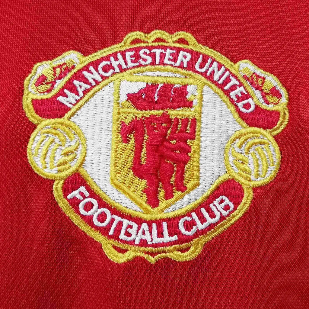 Close-up of the Manchester United Football Club embroidered crest on a red fabric background.