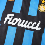 Close-up of a black and light blue striped soccer jersey with the white 'Fiorucci' sponsor logo across the center, a gold Inter Milan crest in the top right, and partial 'Umbro' branding at the top left.
