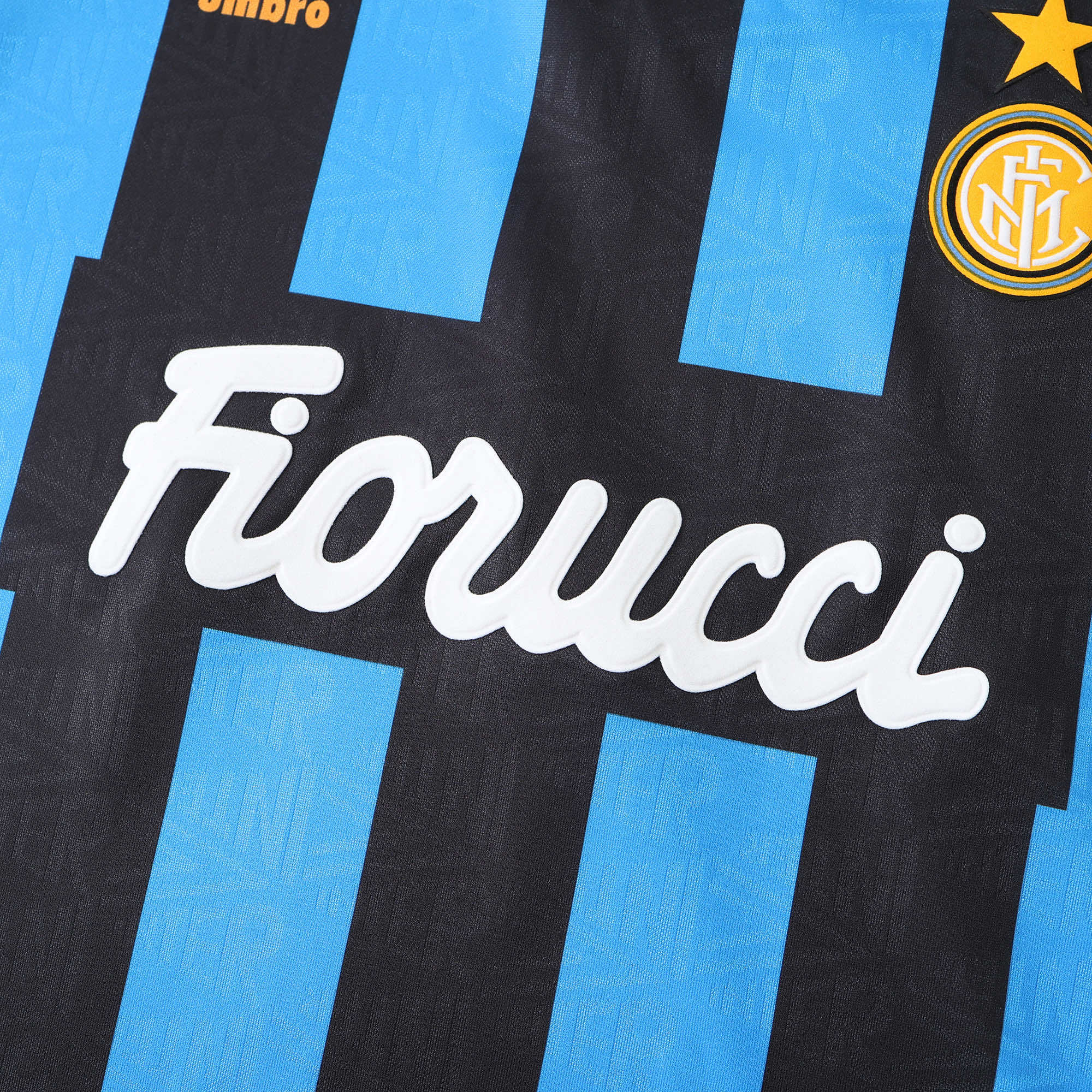 Close-up of a black and light blue striped soccer jersey with the white 'Fiorucci' sponsor logo across the center, a gold Inter Milan crest in the top right, and partial 'Umbro' branding at the top left.