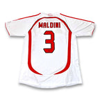 A white soccer jersey shown from the back, featuring the name 'MALDINI' and the number '3' in red with black outlines. The jersey has red trim along the shoulders and sides, set against a plain white background.