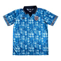 A blue short-sleeve England soccer jersey with a geometric pattern, featuring the Umbro logo on the right chest and the England crest on the left chest, displayed flat against a white background.