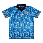 A blue short-sleeve England soccer jersey with a geometric pattern, featuring the Umbro logo on the right chest and the England crest on the left chest, displayed flat against a white background.