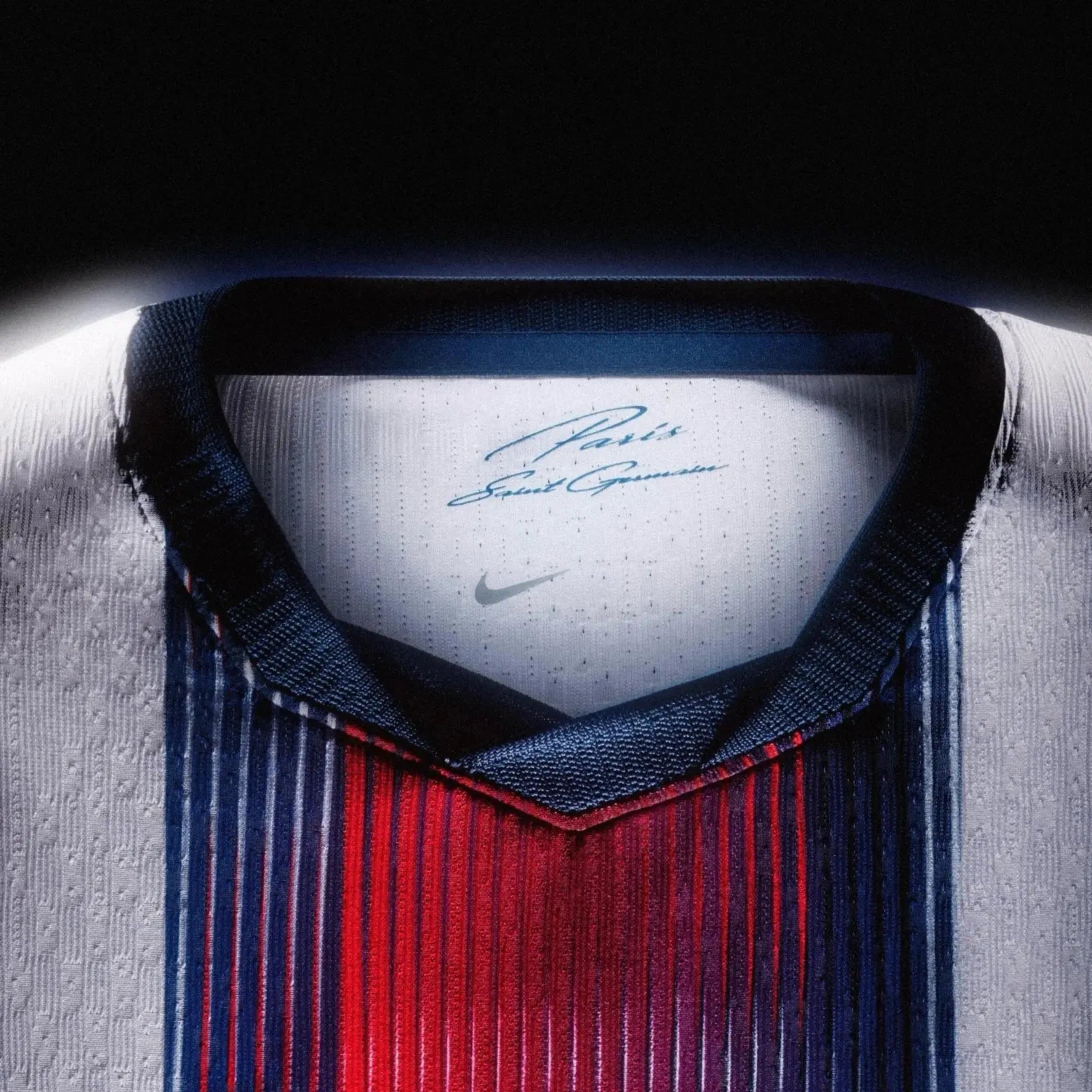 Close-up of a Paris Saint-Germain Nike soccer jersey with vertical navy, red, and white stripes, featuring a white inner collar with a printed player signature and Nike swoosh.