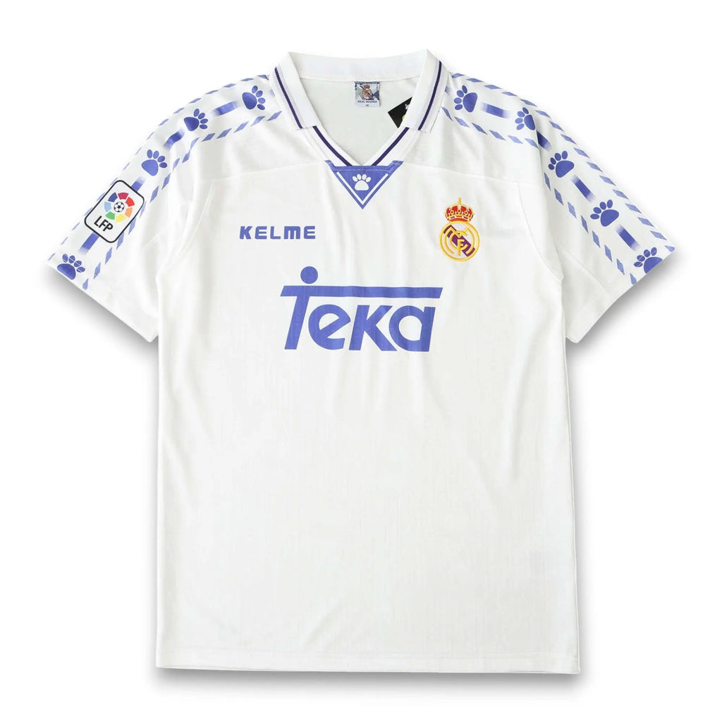 A white Real Madrid soccer jersey by Kelme, featuring blue paw print patterns on the shoulders and sleeves, the blue Teka sponsor logo on the chest, and the club's crest on the left side.