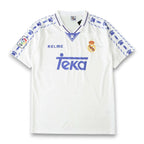 A white Real Madrid soccer jersey by Kelme, featuring blue paw print patterns on the shoulders and sleeves, the blue Teka sponsor logo on the chest, and the club's crest on the left side.
