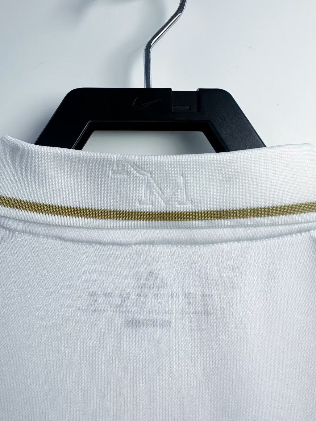 White shirt with a gold trim on a hanger against a white background