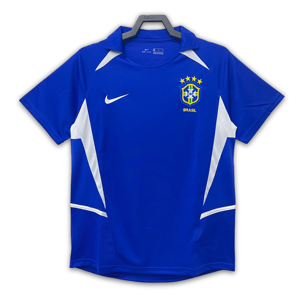 A blue soccer jersey with white accents, featuring the Brazil national team crest, displayed on a white background.