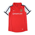 A red Nike Arsenal short-sleeve soccer jersey with white and navy blue sleeve stripes, featuring the 'Dreamcast' sponsor logo on the chest.