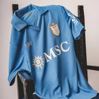 A light blue FC Seoul soccer jersey draped over a dark wooden chair, featuring the white and gold club crest, the sponsor logo 'MSC', and the 'EA' brand mark.