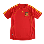 A red Spain national football team Adidas jersey with yellow stripes on the shoulders and sides, featuring the Spain crest on the chest, displayed against a solid black background.