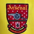 Elite Retro Kits Arsenal 1993/94 away shirt crest featuring the cannon emblem on a yellow textured fabric background