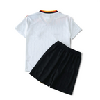 Elite Retro Kits Germany 1994 kids home football kit with white jersey and black shorts on a green pitch background