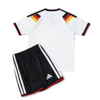 Elite Retro Kits Germany 2026 kids home kit featuring a white jersey with flag-colored shoulders and black shorts.