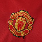 Elite Retro Kits Manchester United 2005/06 kids home kit featuring a detailed embroidered club crest on red fabric.