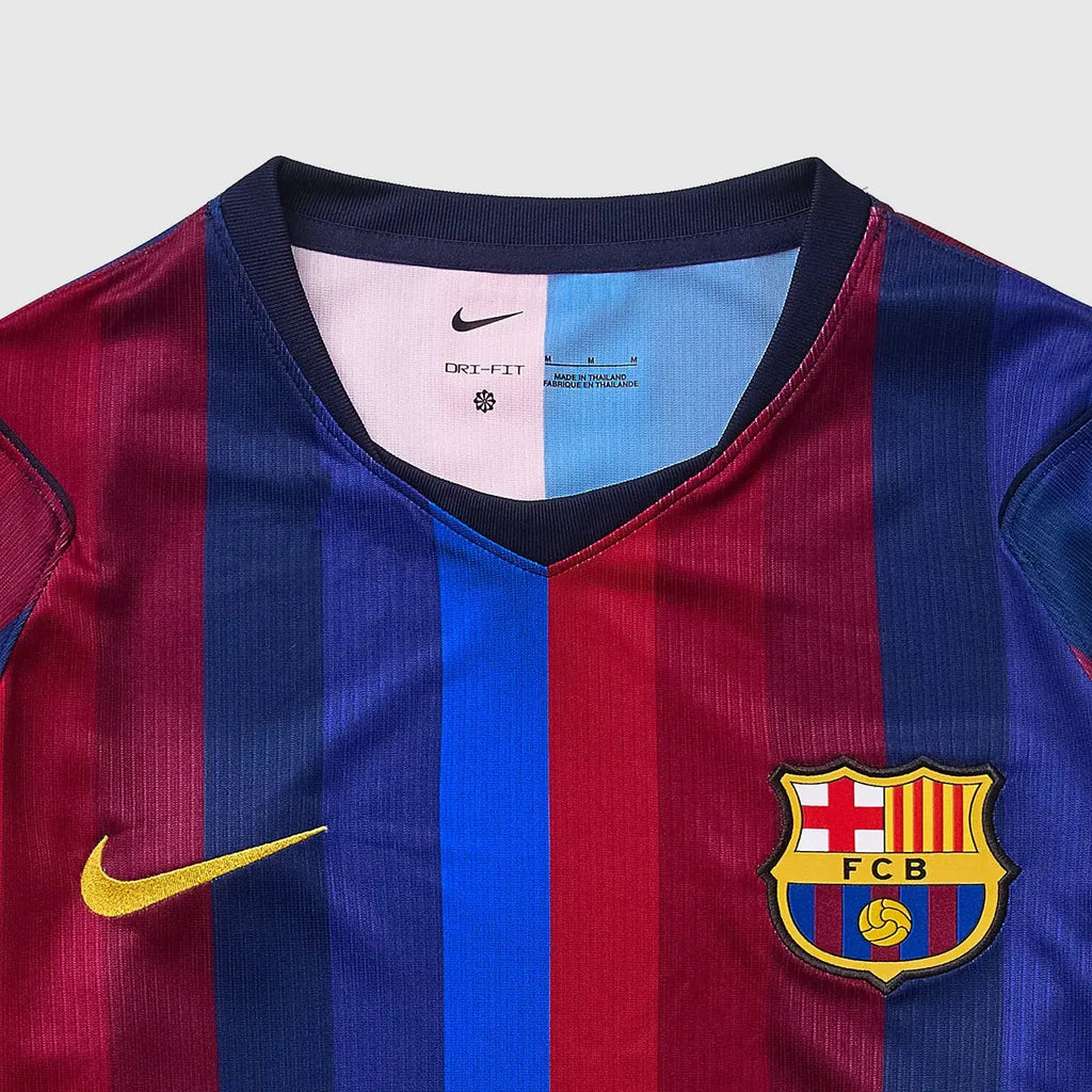 Close-up of a Nike FC Barcelona home soccer jersey with vertical blue and red stripes, a yellow Swoosh on the right chest, and the FC Barcelona crest on the left chest.