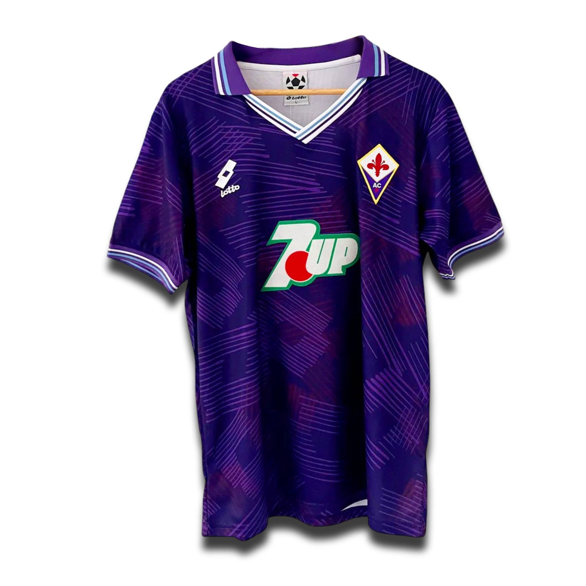 A vintage soccer jersey in purple with a geometric pattern, featuring the original Lotto logo, a collar, and 7UP sponsor branding.