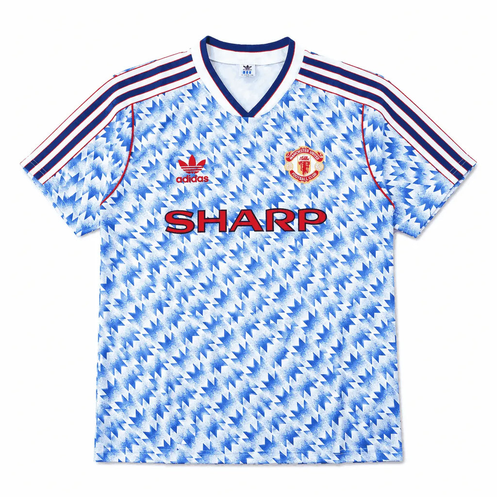 A vintage Manchester United home soccer jersey by Adidas, featuring a light blue and white geometric pattern, navy blue and red shoulder stripes, the red Adidas logo, the Manchester United crest, and the red SHARP sponsor text.