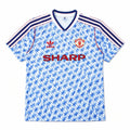 A vintage Manchester United home soccer jersey by Adidas, featuring a light blue and white geometric pattern, navy blue and red shoulder stripes, the red Adidas logo, the Manchester United crest, and the red SHARP sponsor text.
