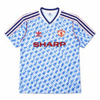A vintage Manchester United home soccer jersey by Adidas, featuring a light blue and white geometric pattern, navy blue and red shoulder stripes, the red Adidas logo, the Manchester United crest, and the red SHARP sponsor text.