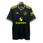 Black Manchester United jersey with yellow accents and brand logos on a white background