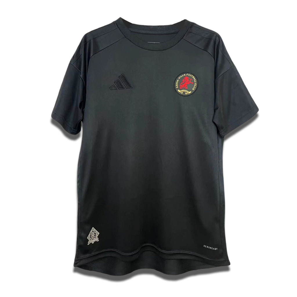A black Aston Villa shirt with a crest and logo on the front, along with a small badge on the lower right. It features short sleeves and a round neckline.