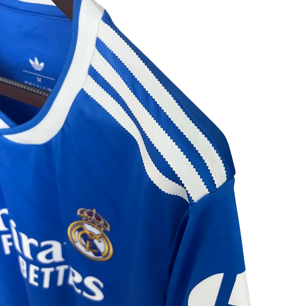 Blue Real Madrid jersey with white stripes and logos on a hanger