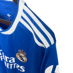 Blue Real Madrid jersey with white stripes and logos on a hanger