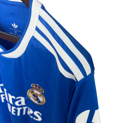 Blue Real Madrid jersey with white stripes and logos on a hanger