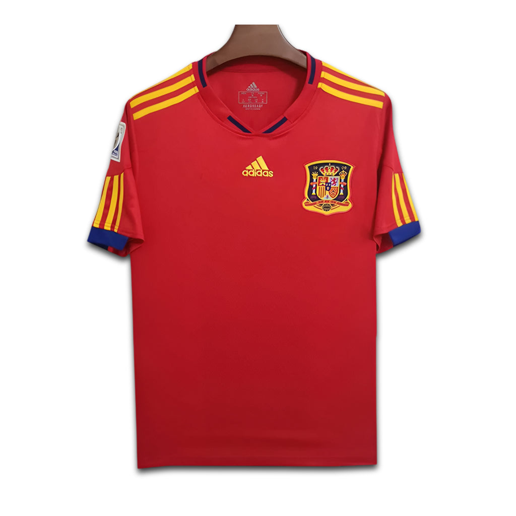 Red sports jersey with yellow and blue accents, featuring an Adidas logo and a crest on a white background.
